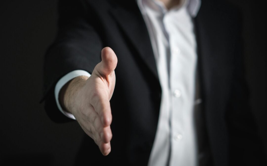 A business person in a suit reaching out to shake hands with you to complete a business law deal.