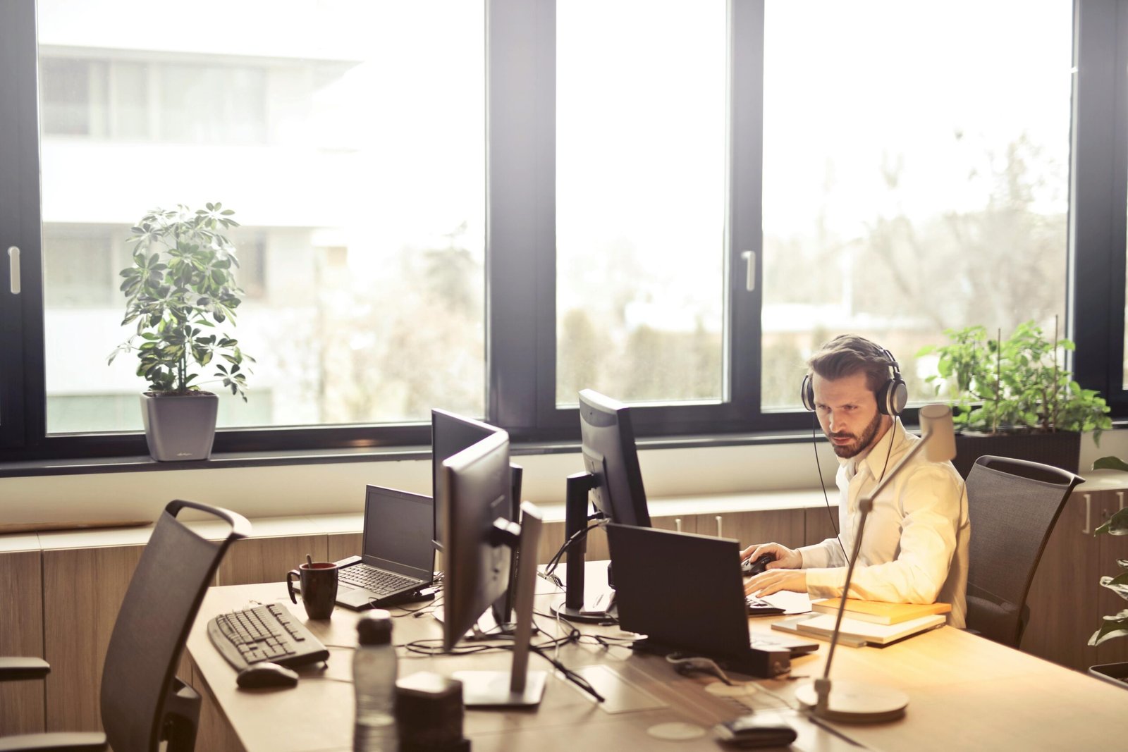 A man on a computer in a sunny office wearing a headset.